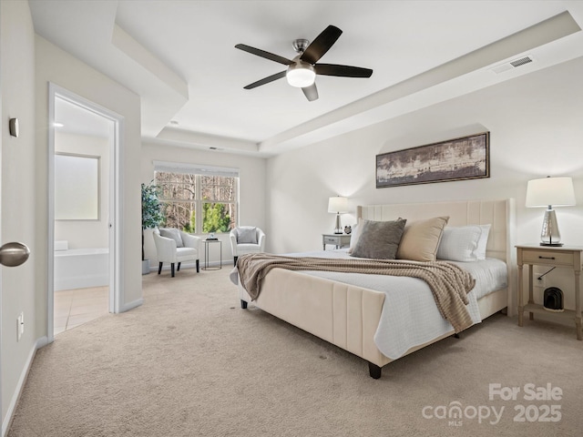 bedroom featuring ceiling fan, ensuite bathroom, light carpet, and a tray ceiling