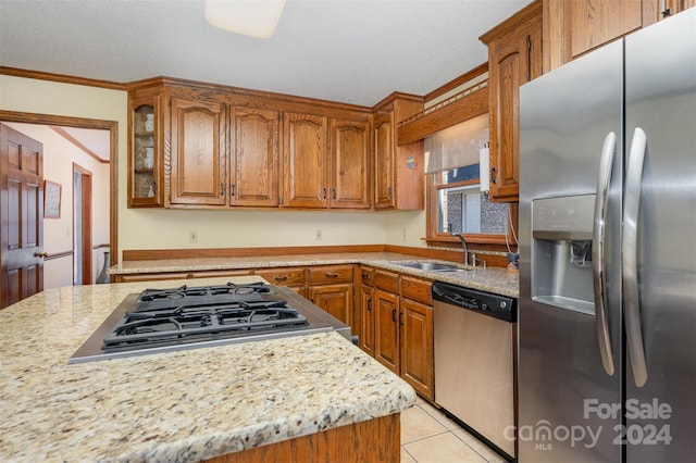 kitchen with sink, ornamental molding, light tile patterned floors, light stone counters, and stainless steel appliances