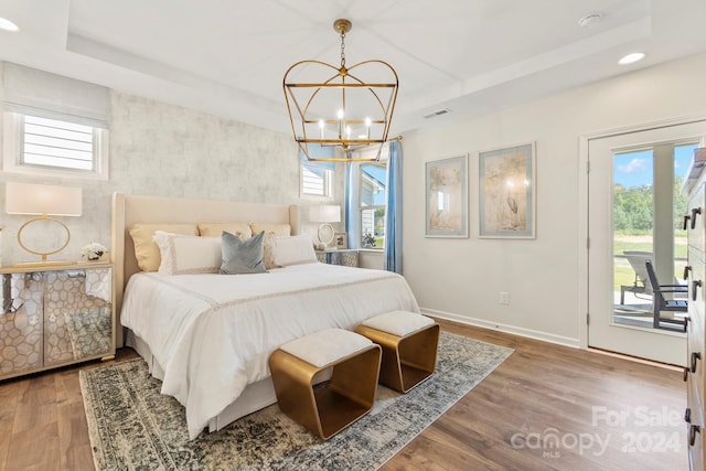 bedroom with hardwood / wood-style flooring, a notable chandelier, access to exterior, and a tray ceiling