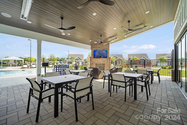 view of patio with an outdoor brick fireplace, ceiling fan, and a community pool