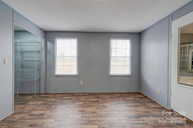 empty room with dark hardwood / wood-style flooring, a textured ceiling, and a healthy amount of sunlight