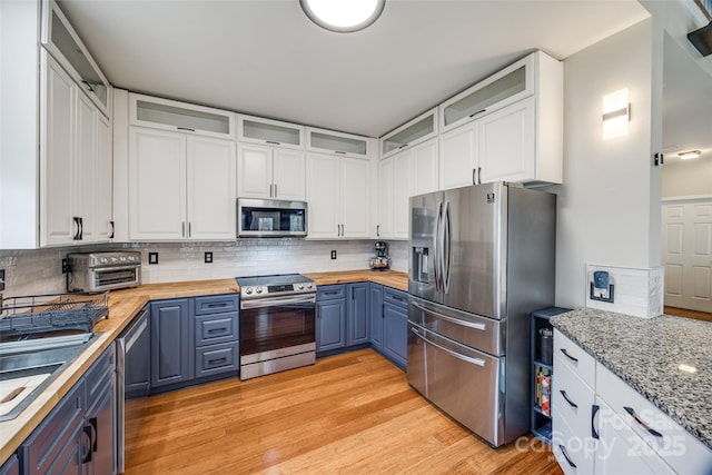 kitchen with light wood-type flooring, blue cabinetry, appliances with stainless steel finishes, white cabinetry, and butcher block counters