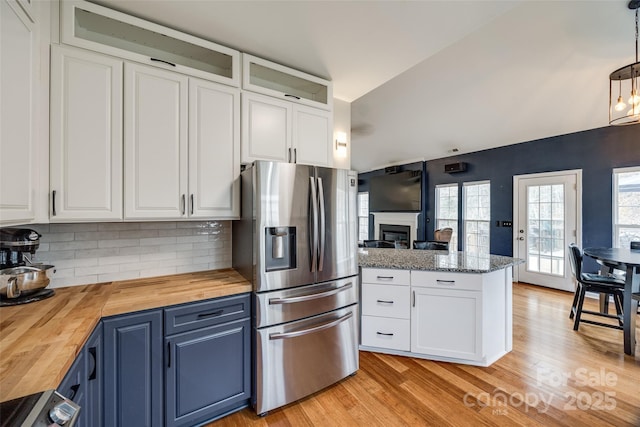 kitchen with stainless steel refrigerator with ice dispenser, wood counters, blue cabinetry, hanging light fixtures, and white cabinets