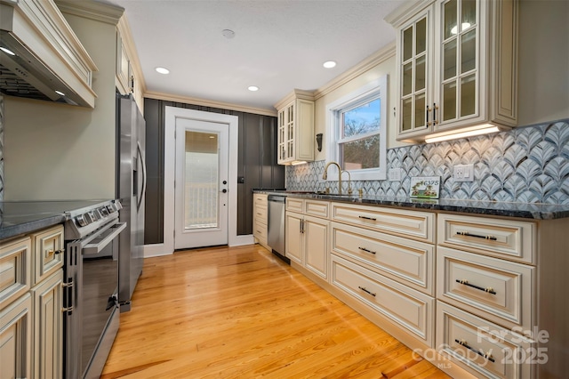 kitchen featuring light hardwood / wood-style flooring, premium range hood, appliances with stainless steel finishes, cream cabinetry, and dark stone counters