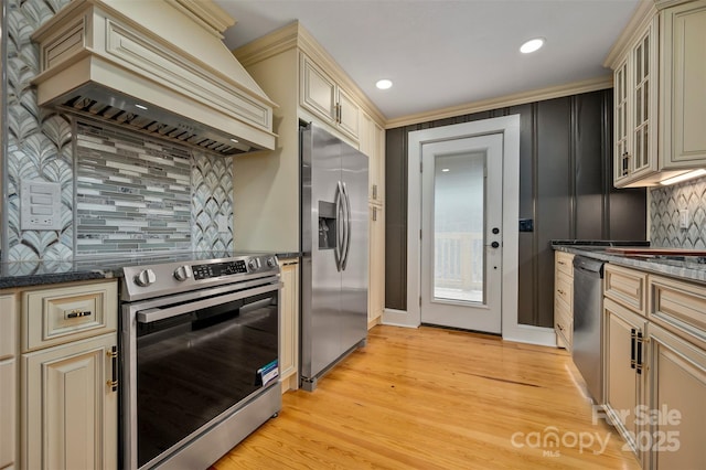 kitchen featuring premium range hood, cream cabinets, stainless steel appliances, light hardwood / wood-style floors, and decorative backsplash