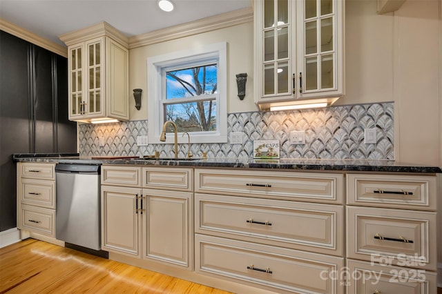 kitchen with sink, dark stone countertops, stainless steel dishwasher, cream cabinets, and light hardwood / wood-style flooring