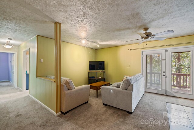 carpeted living room featuring french doors, ceiling fan, wooden walls, and a textured ceiling