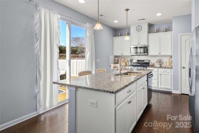 kitchen with sink, dark stone countertops, appliances with stainless steel finishes, pendant lighting, and a kitchen island with sink