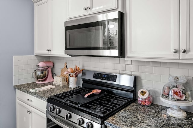 kitchen with appliances with stainless steel finishes, dark stone countertops, white cabinets, and backsplash