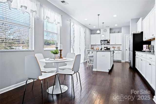 kitchen with an island with sink, stone countertops, white cabinets, and decorative light fixtures