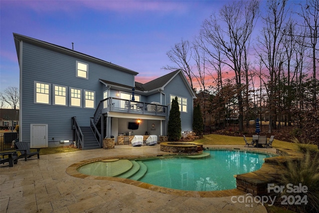 back house at dusk with a patio area, a balcony, and a pool with hot tub