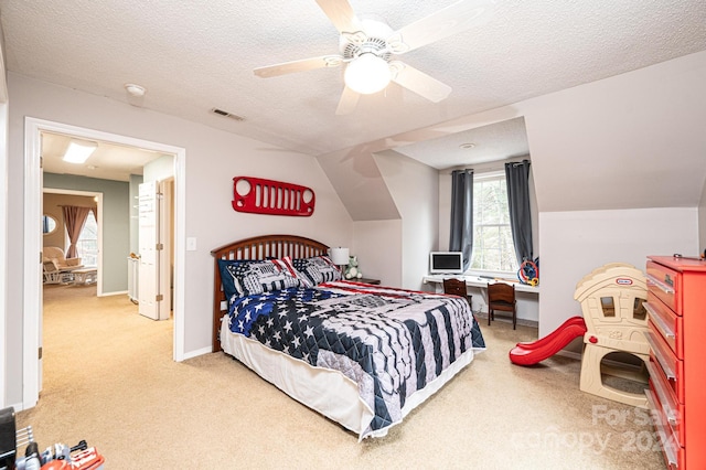 bedroom with a textured ceiling, light colored carpet, vaulted ceiling, and ceiling fan