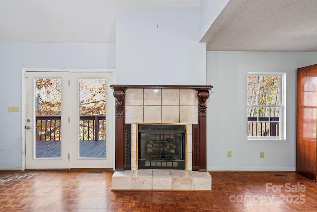 unfurnished living room featuring a textured ceiling, dark parquet floors, a fireplace, and a wealth of natural light