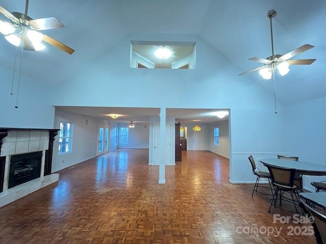 living room featuring dark parquet flooring, ceiling fan, high vaulted ceiling, and a tiled fireplace