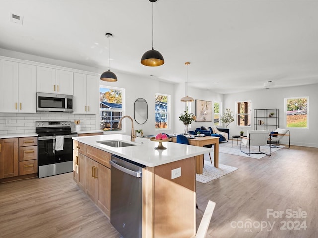 kitchen with a kitchen island with sink, white cabinets, sink, light hardwood / wood-style flooring, and stainless steel appliances