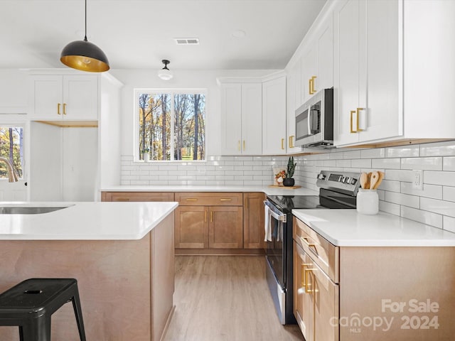 kitchen with white cabinetry, sink, light hardwood / wood-style floors, decorative light fixtures, and appliances with stainless steel finishes