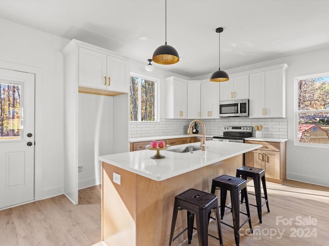 kitchen featuring white cabinets, a healthy amount of sunlight, a center island with sink, and stainless steel appliances