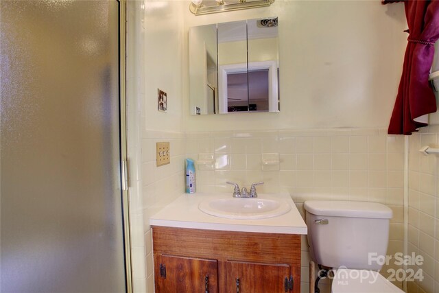 bathroom with tile walls, vanity, an enclosed shower, and toilet