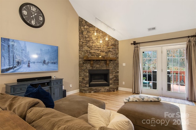 living room with track lighting, a stone fireplace, high vaulted ceiling, and light hardwood / wood-style flooring