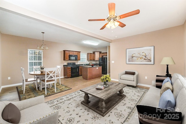 living room featuring ceiling fan with notable chandelier and light hardwood / wood-style flooring