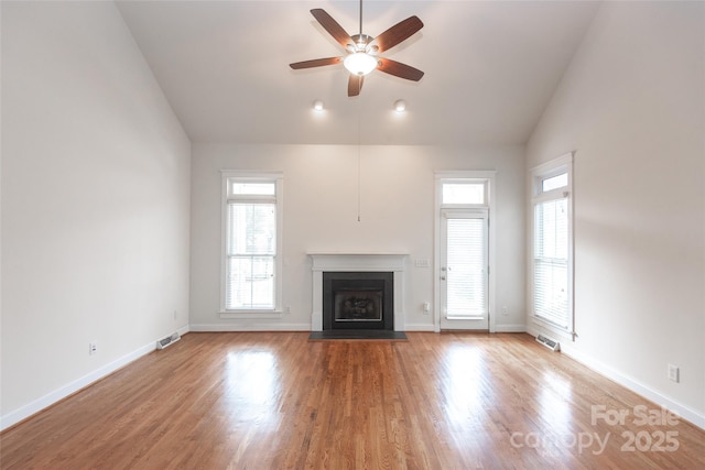 unfurnished living room with ceiling fan, a healthy amount of sunlight, vaulted ceiling, and light wood-type flooring