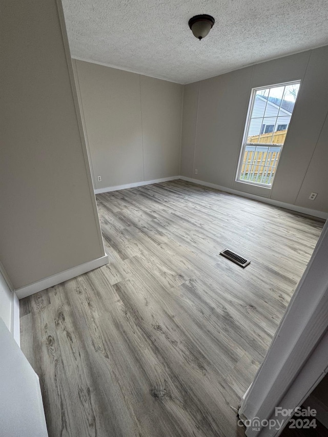 spare room with light wood-type flooring and a textured ceiling