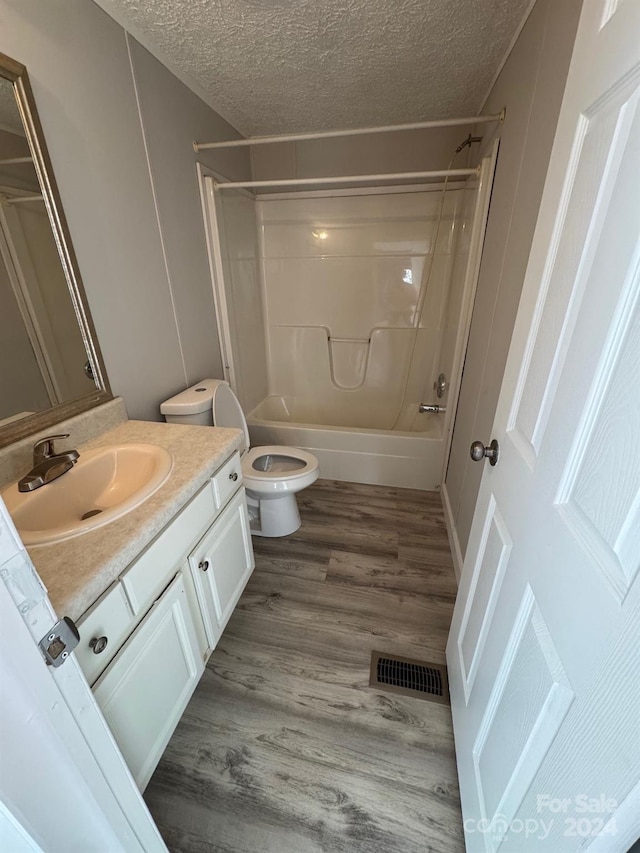 full bathroom featuring hardwood / wood-style floors, a textured ceiling, toilet, shower / washtub combination, and vanity