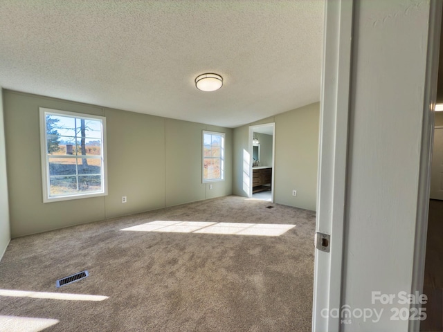 unfurnished bedroom with ensuite bath, carpet floors, and a textured ceiling