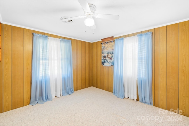 unfurnished room featuring carpet floors, a wealth of natural light, and wooden walls