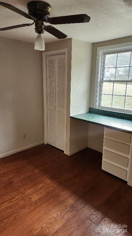 unfurnished bedroom featuring ceiling fan, dark hardwood / wood-style floors, built in desk, a textured ceiling, and a closet