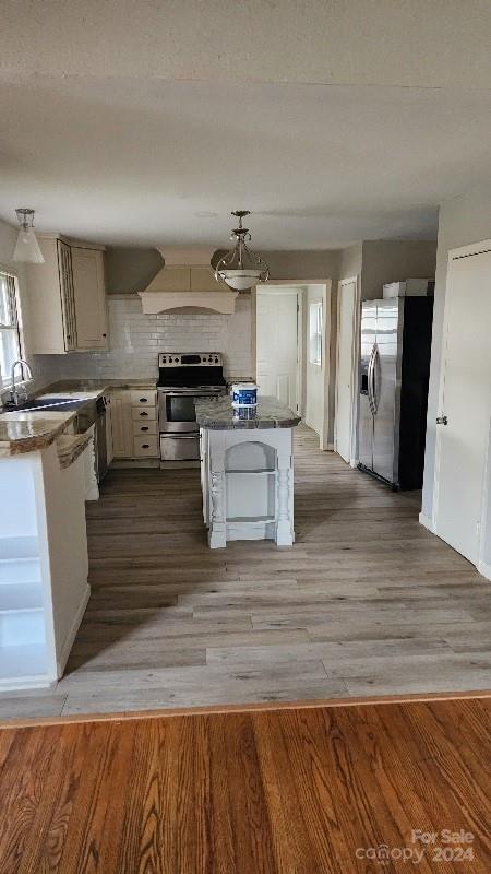 kitchen featuring decorative backsplash, premium range hood, stainless steel appliances, sink, and light hardwood / wood-style floors