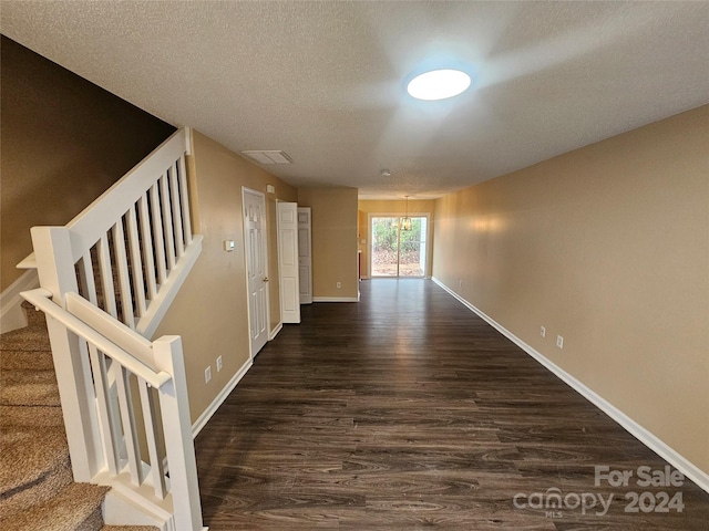 hallway with dark hardwood / wood-style floors, a textured ceiling, and a chandelier