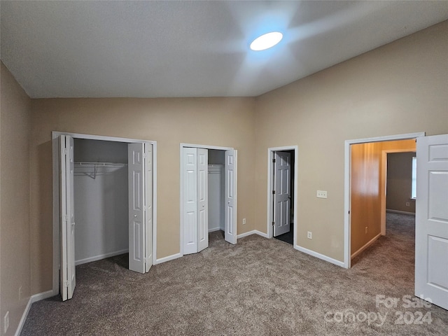 unfurnished bedroom featuring carpet flooring, vaulted ceiling, and multiple closets