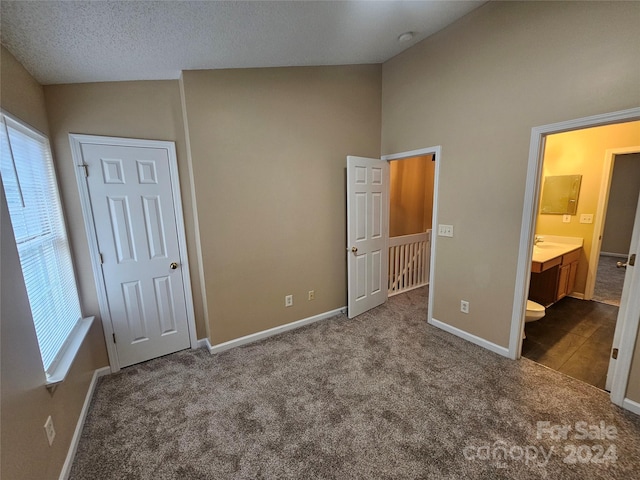 unfurnished bedroom with ensuite bath, sink, a textured ceiling, vaulted ceiling, and carpet