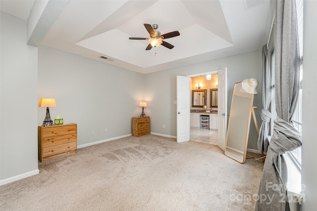 bedroom with ensuite bathroom, a raised ceiling, ceiling fan, and light colored carpet