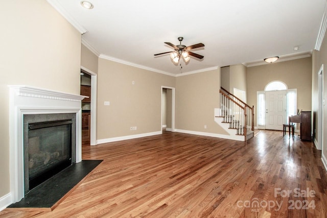 131 Quail Haven Dr, Troutman, NC 28166 - unfurnished living room with stairs, wood finished floors, a ceiling fan, crown molding, and a glass covered fireplace