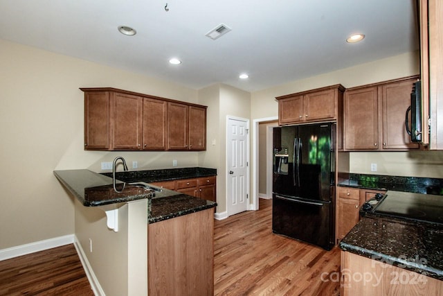 kitchen featuring black appliances, dark stone countertops, sink, and light hardwood / wood-style flooring