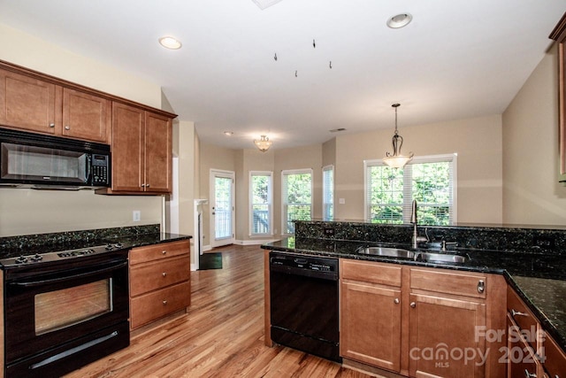 kitchen with light wood-type flooring, sink, black appliances, pendant lighting, and dark stone countertops