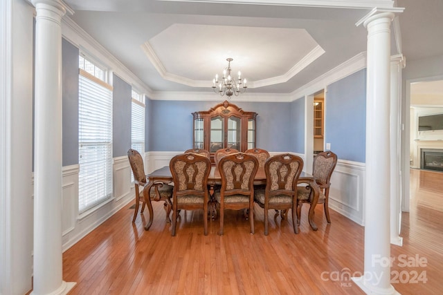 dining space with crown molding, light hardwood / wood-style flooring, ornate columns, a tray ceiling, and a notable chandelier