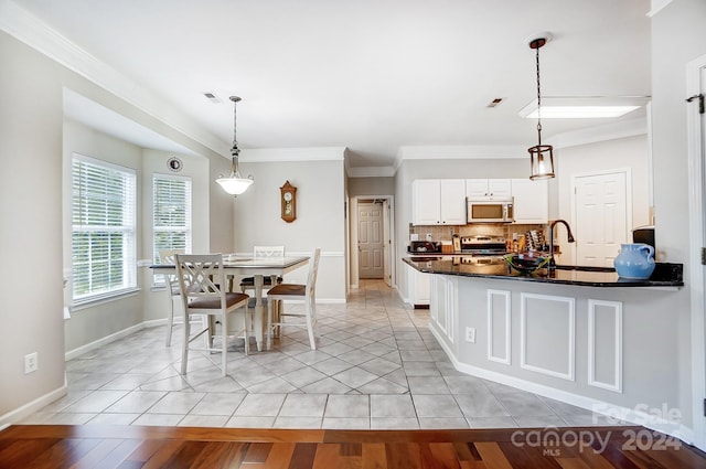 kitchen featuring backsplash, white cabinets, hanging light fixtures, light wood-type flooring, and stainless steel appliances