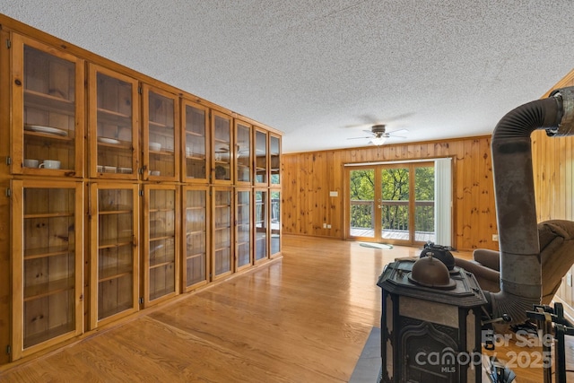 interior space with ceiling fan, light wood-type flooring, wooden walls, and a wood stove