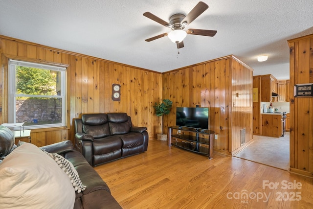 living room with ceiling fan, light hardwood / wood-style flooring, wood walls, a textured ceiling, and ornamental molding