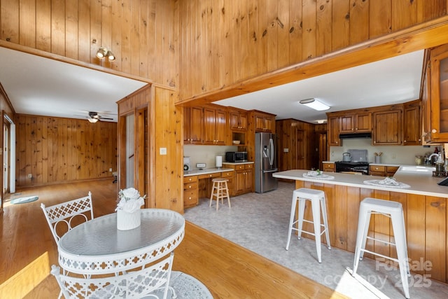 kitchen with kitchen peninsula, appliances with stainless steel finishes, a kitchen breakfast bar, sink, and wood walls