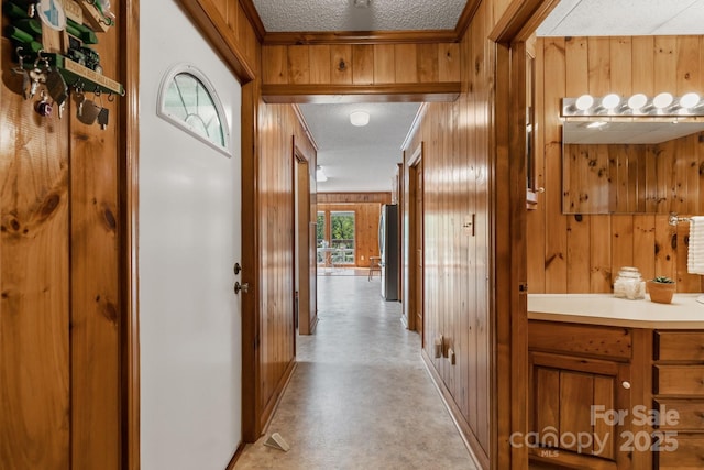 hallway with a textured ceiling, wood walls, and crown molding