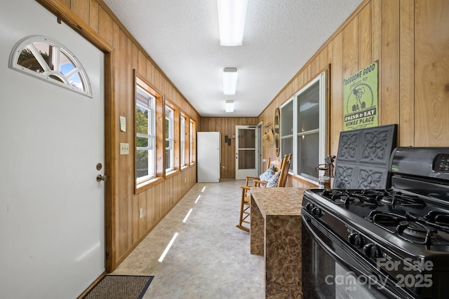 kitchen featuring black gas stove, a textured ceiling, and wood walls