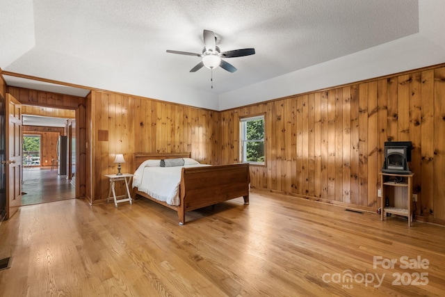 bedroom with wooden walls, light hardwood / wood-style flooring, ceiling fan, stainless steel fridge, and a textured ceiling