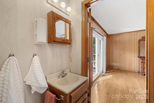 bathroom with ornamental molding, vanity, a textured ceiling, hardwood / wood-style floors, and wood walls