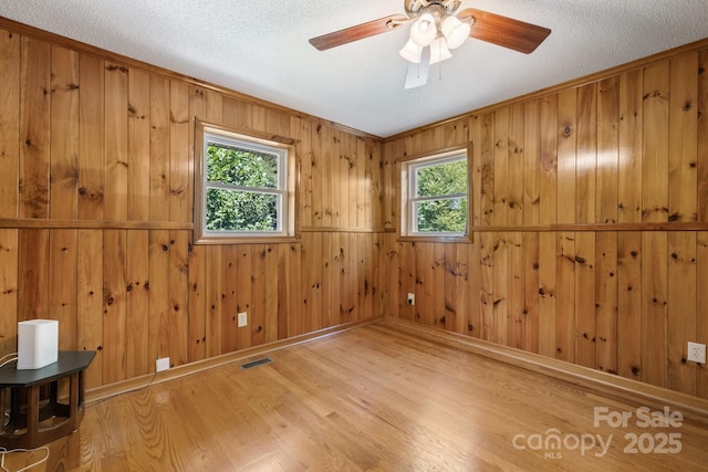 spare room featuring ceiling fan, wood walls, a textured ceiling, and light hardwood / wood-style flooring