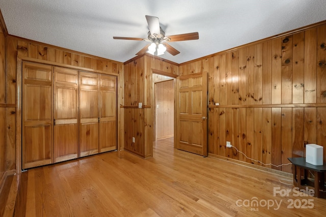 unfurnished bedroom featuring ceiling fan, light wood-type flooring, crown molding, and a closet