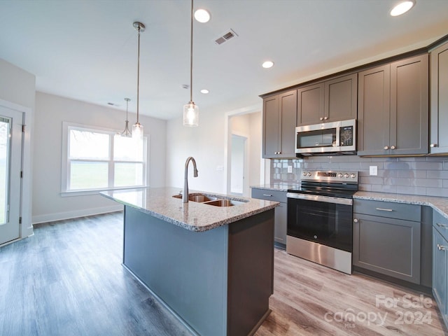 kitchen with appliances with stainless steel finishes, a center island with sink, light hardwood / wood-style flooring, and sink